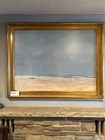 Full view of large framed coastal print hung above a stone fireplace mantle.