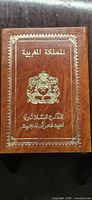 Front cover of the leather-bound stamp booklet with gold embossed Moroccan emblem and Arabic script.
