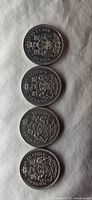 Four Canadian half dollar coins showing the coat of arms side stacked vertically on white cloth.