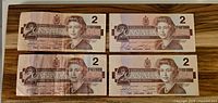 Front side of four Canadian $2 bills showing Queen Elizabeth II portrait and denomination markings.