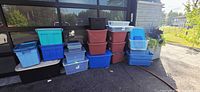 Assorted plastic storage totes of various sizes and colors arranged against a stone wall outdoor