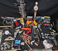 Full overview of assorted tools laid out on black fabric background including hand tools, power tools, plumbing fittings, and fasteners.