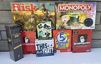 Photo showing Risk, Monopoly Voice Banking, Scattergories (two editions), 5 Second Rule, This or That, As Ode!, and a Clue game box all arranged together outdoors.