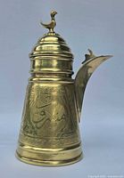 Front view of the brass dallah showing the engraved patterns and bird finial on the lid.