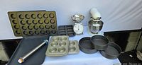 Overview of bakeware including trays with different sized molds and pans, KitchenAid mixer in background, and kitchen scale.