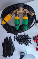 Photo showing brass hose splitter with two yellow-green valves attached to coiled black irrigation hose, black stakes, and drip emitters below.