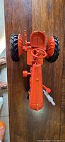 Top view of the red/orange die-cast model tractor showing the steering wheel, large rubber rear tires, and detailed engine body.