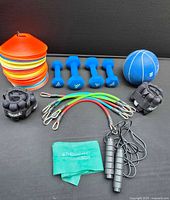 Full overview of all exercise equipment including dumbbells, weights, resistance bands, agility cones, jump rope, and medicine ball on black background
