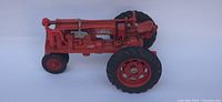 Side view of the red Farmall diecast tractor model showing detailed engine and tires, with large rear rubber tires and smaller front tires.
