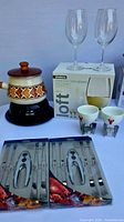 Photo showing vintage ceramic fondue pot with burner, two wine glasses, and two boxed lobster utensil sets