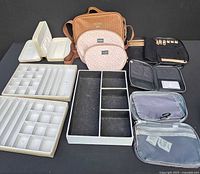 Overview of Guess travel bags, jewelry trays, and organizers laid out on black surface showing bag shapes, trays and pouches.