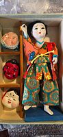 Photo of the antique Japanese doll dressed in traditional clothing with three traditional masks displayed beside it in a box.