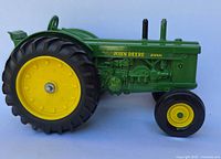 Side view of the left side of the John Deere diecast tractor showing detailed engine parts, decals and large rear tire with yellow wheel.