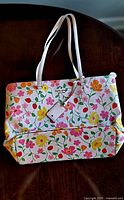 Front view of a rectangular handbag with white shoulder straps and colorful floral-strawberry print