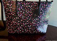 Front view of the Kate Spade New York Schuyler tote bag showing the black faux leather with a vibrant floral pattern and double handles.
