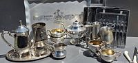 Close-up side view highlighting ornate silver teapot, sugar bowls, creamers, goblets, cups with gold interior and serving trays behind