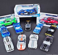 Overview photo showing 12 die cast model cars on a black surface including three boxed and nine unboxed cars arranged in front.