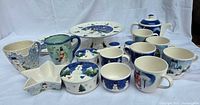 Photo showing the entire set of holiday dishes with snowman and winter themed designs, including mugs, teapot, pedestal cake plate, star dish, and covered dish.