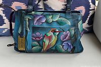Front view of Anuschka hand-painted leather bag with detailed colorful bird and flower design in blue and purple tones