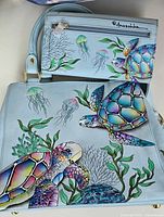 Photo showing light blue genuine leather shoulder bag and matching wallet with colorful sea turtles, jellyfish, and marine life hand-painted designs
