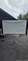 Front view of the white projector screen on tripod stand outdoors.