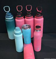 Image of seven insulated bottles and a tumbler with carrying handles and lids, displayed against a black background.