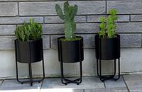 Set of three black metal planters with green cacti placed on a tiled floor in front of a stone wall.