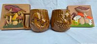 Front view of two mushroom mugs and two mushroom wall plaques against white background.