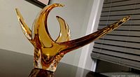 Angled shot of the amber hand-blown glass sculpture showing three main spiked elements extending upward and outward.