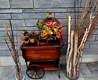 Full view of vintage wooden tea cart with two glass cylindrical vases filled with twigs and branches, and seasonal fall decor on top of the cart