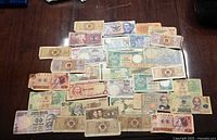 Image showing a variety of banknotes spread on a table from multiple countries including South Korea, Vietnam, Mexico, and Yugoslavia. Notes vary in colors, size, and wear, many appear older with signs of heavy usage.