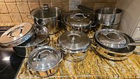 Multiple stainless steel pots and pans with lids arranged on countertop