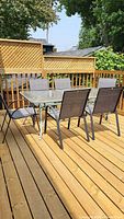 Full view of the 6-seater glass and metal outdoor patio table set on wooden deck, showing rectangular glass table with six matching chairs.