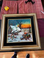 Full view of framed painting on glass showing winter scene with cottages, trees and figures, measuring approximately 18x24 inches with black velvet matting and gold frame.