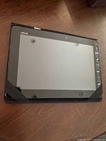 Front view of ASUS Android tablet in a case, screen visible with reflective surface.