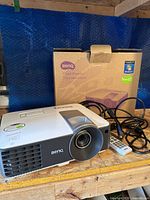 BenQ projector, remote, power cable on wooden shelf with box in background