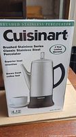 Front of the Cuisinart brushed stainless steel percolator box showing branding and key features like superior heat retention and brewing capacity.