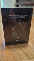 Front of box showing image of smartwatch with colorful digital display and text 'Track & Monitor Your Vitals SMARTWATCH'.