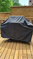 Grill covered with black protective cover on wooden deck