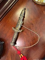 Decorative ornate dagger sheathed on wooden surface showing embossed designs and tassel.