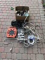 Overall lot on brick surface showing multiple power bars, extension cords coiled and loose, HDMI cables, video cables, and orange cable reel.