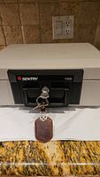Front view of Sentry 1100 safe showing lock with two keys attached to a leather keychain.