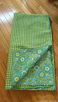 Folded green floral patterned blanket showing reversed blue floral and paisley pattern with quilting textures