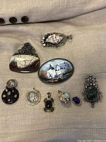 Overview photo of assorted eclectic necklaces and pendants laid out on fabric, including ceramic stone, painted scene, and silver items