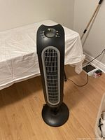 Full view of the Honeywell tower fan heater, upright on floor with black and gray body and vertical front vent grille.