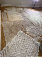 Photo showing large lace and crochet pieces spread on floor, including rectangular and oval table runners with intricate designs.