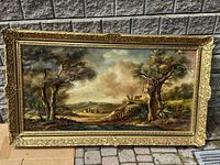 Full view of the large horizontal oil painting in ornate gilt frame showing pastoral countryside scene with trees, village, and figure with livestock.