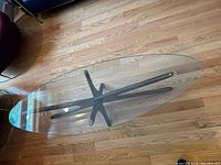 Top-down view of oval glass top and X-shaped wooden base on hardwood floor