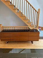 Full front view of sideboard under staircase showing wood veneer finish, glass top and steel legs.