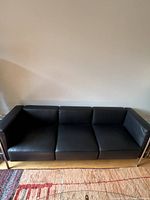 Front view of entire sofa showing three seat cushions, straight arms and black leather upholstery.